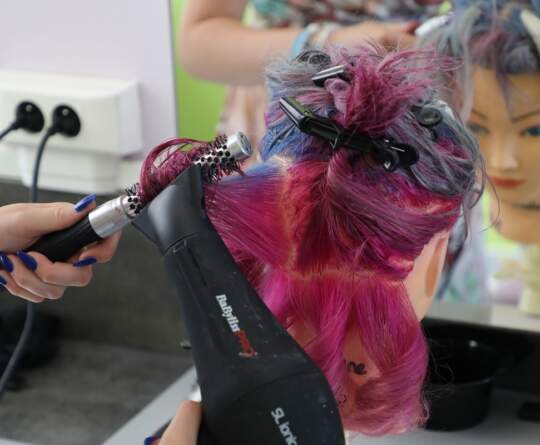 Coiffeuse qui coiffe des cheveux roses et bleus.